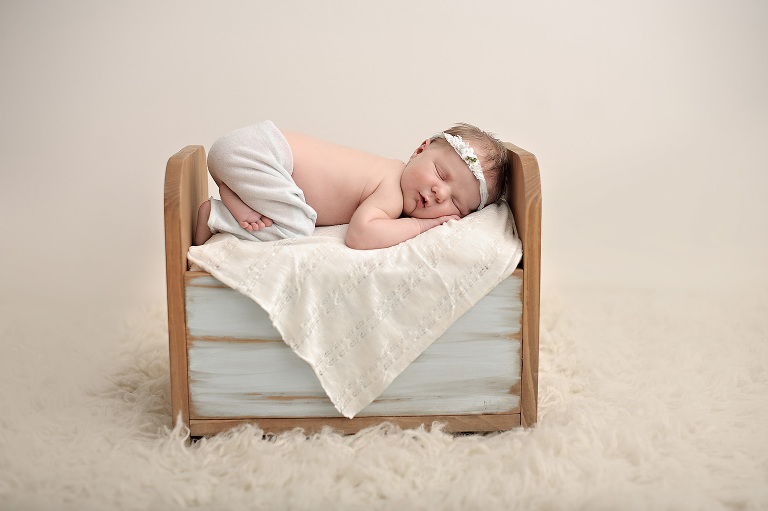 Cream fur rug with newborn girl tushie up in mint baby bed