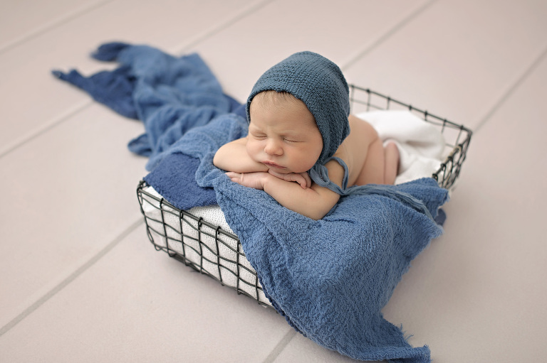Perfect newborn in wire basket with blue wrap layers and a blue bonnet