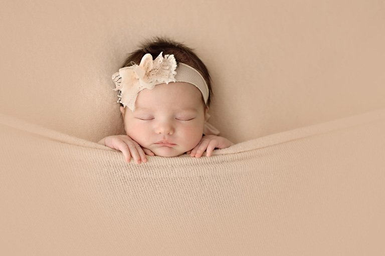 Newborn baby girl tucked in tight with peach blanket and peaches and cream headband