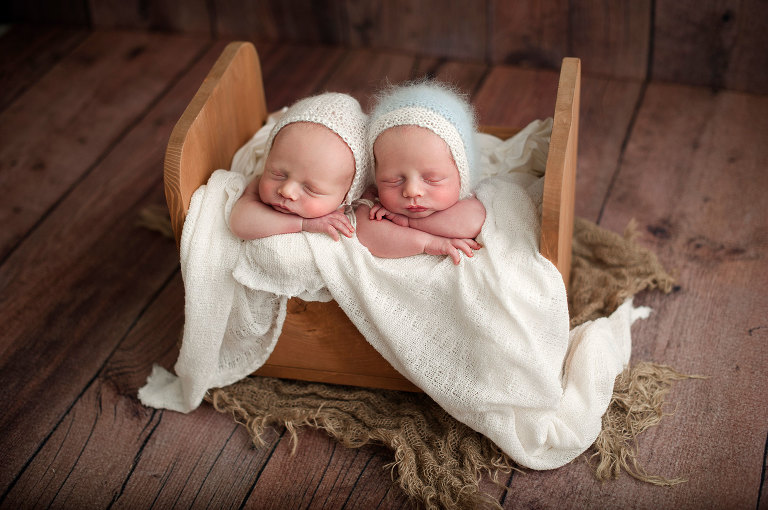 Twin newborn boys in tiny bed with mohair bonnets