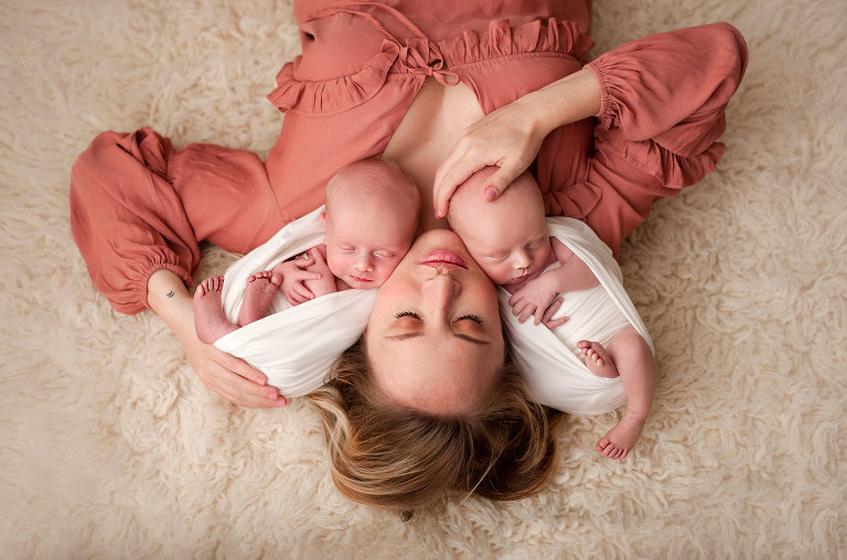 Mama in rust color dress with newborn twin boys on cream rug
