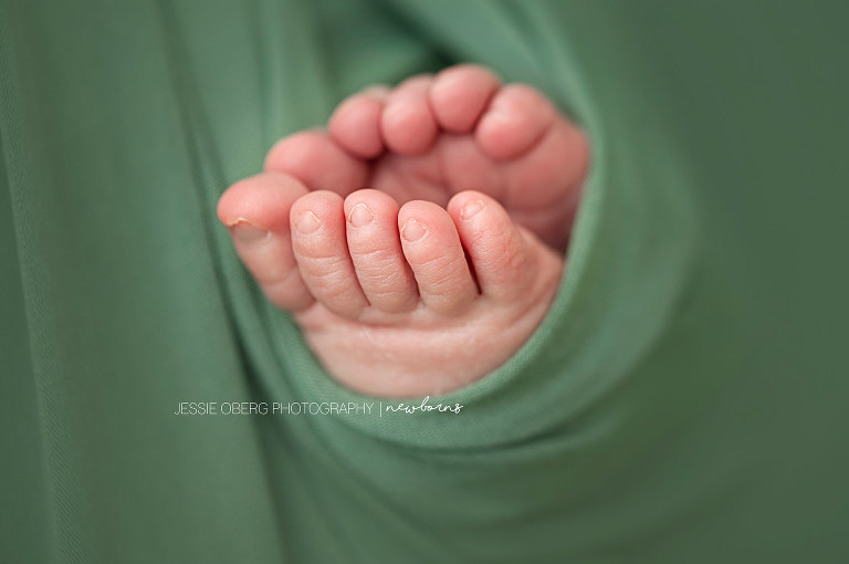 Macro shot of newborn baby's toes wrapped up in green blanket.