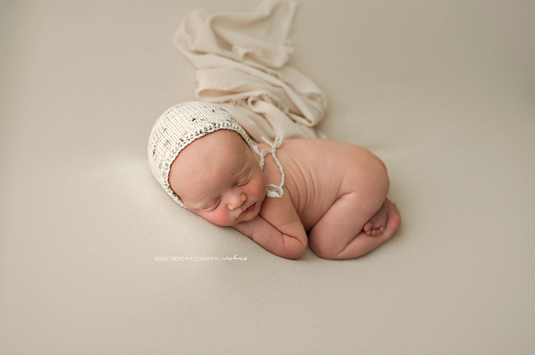 Baby boy posed on cream backdrop with speckled bonnet.